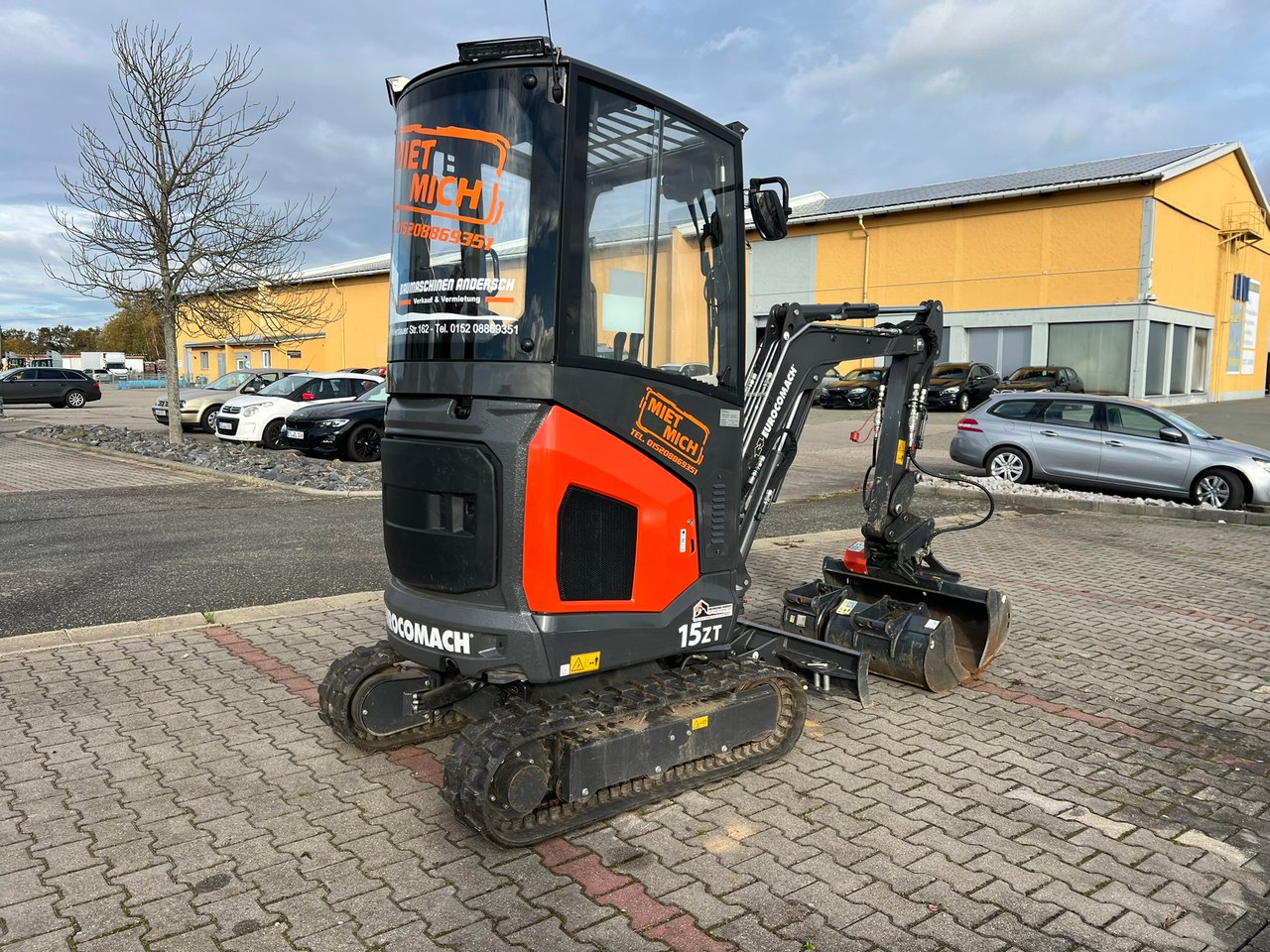 Schwarzer und oranger Minibagger mit der Aufschrift „WETTLICH“ und „1.5ET“ auf einem Parkplatz.