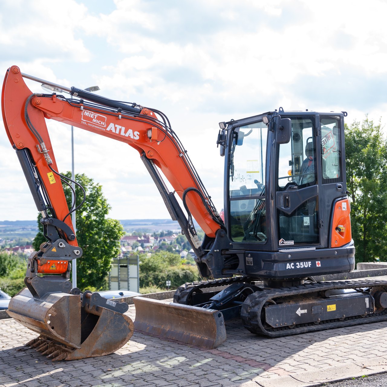 Oranger Atlas Minibagger AC 35UF mit Raupenfahrwerk und Schaufel auf asphaltiertem Parkplatz.