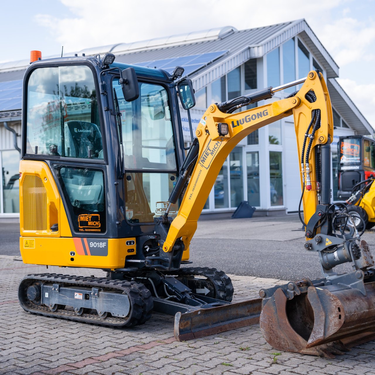 Ein gelber LiuGong B018F Minibagger mit schwarzem Fahrerhaus und Ketten steht auf Pflastersteinen.